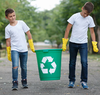 Two boys with yellow cleaning gloves, carrying a recycling bin together