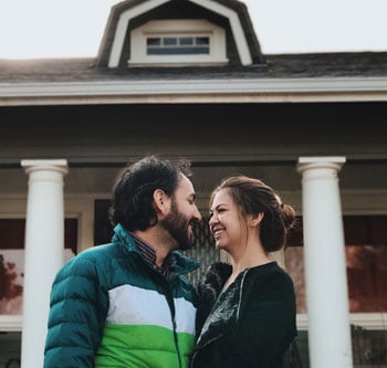 Man and woman looking at each other lovingly in from of a home