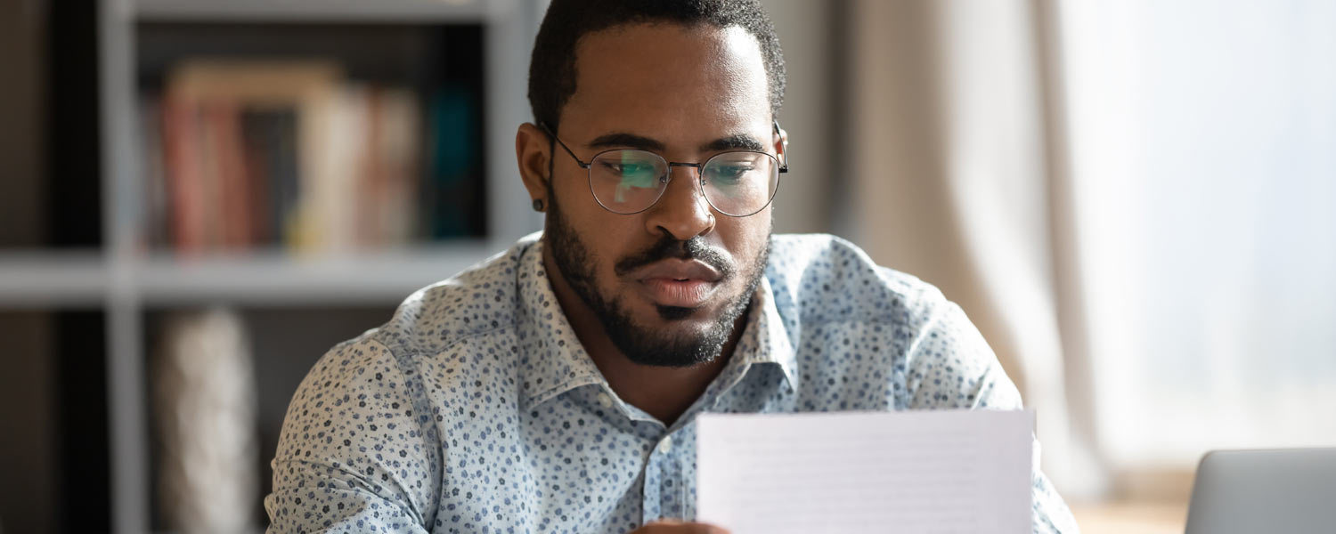 Man in glasses staring pensively at a piece of paper